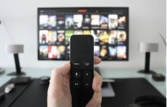A hand holding a remote control in front of a television

Description automatically generated